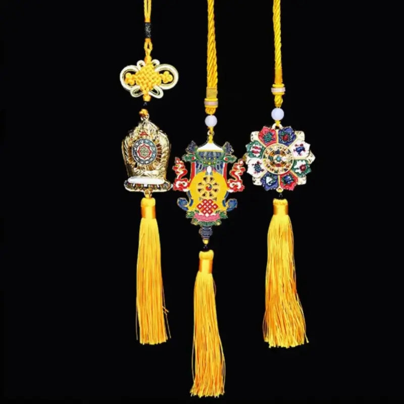 Three Tibetan lucky charm tassels featuring colorful auspicious metal emblems and long yellow silk fringes on black background.