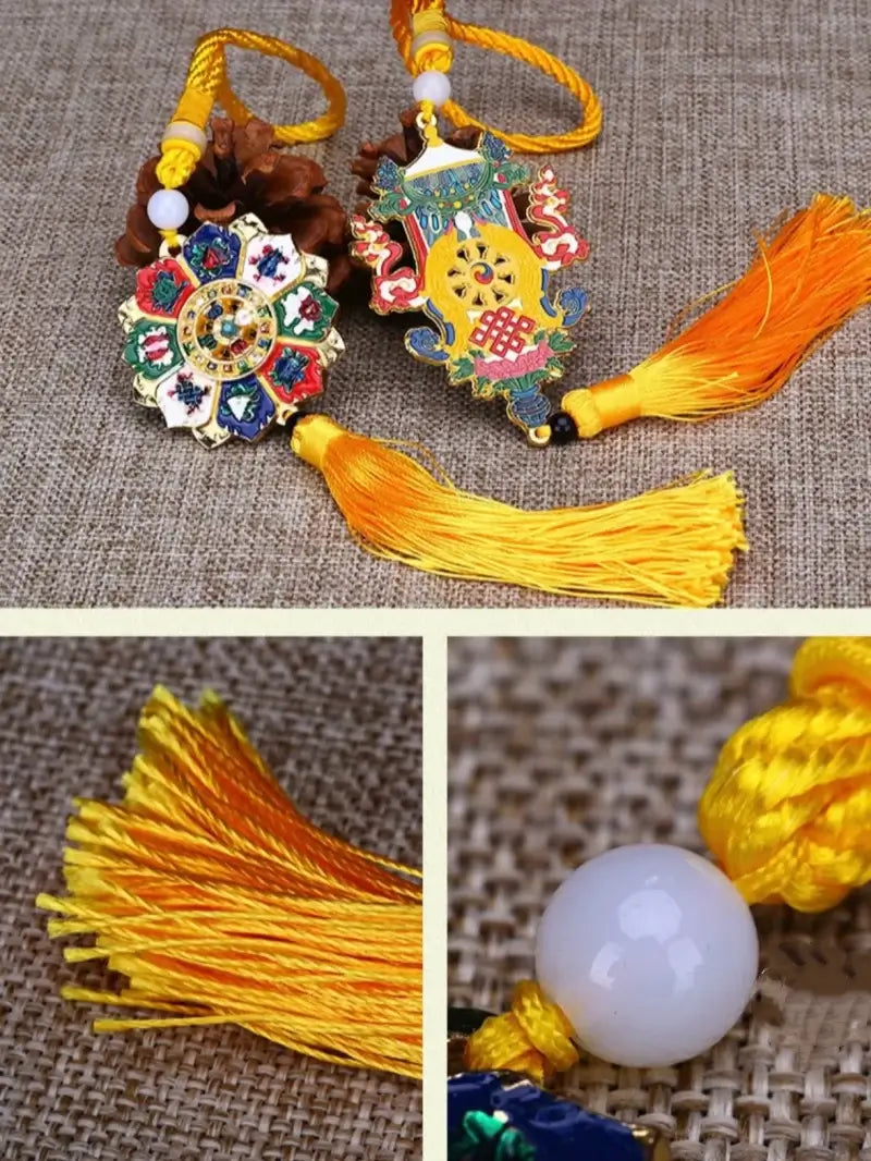 Tibetan car hanging pendants featuring enamel emblems, yellow tassels, and white jade accent beads on a textured fabric.