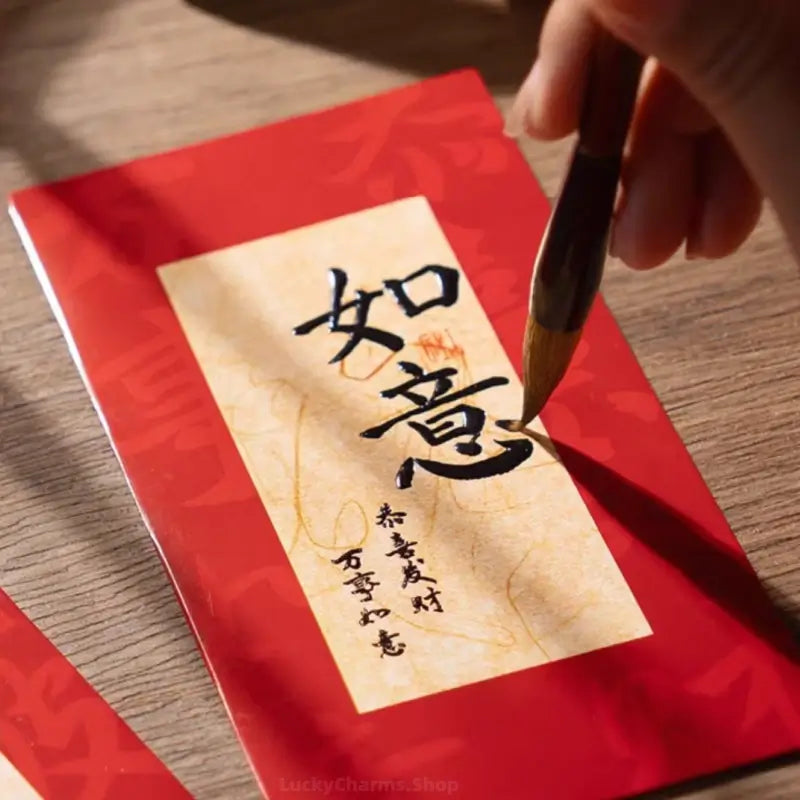 Close-up of hand painting Chinese calligraphy brush characters on a red envelope with parchment center.