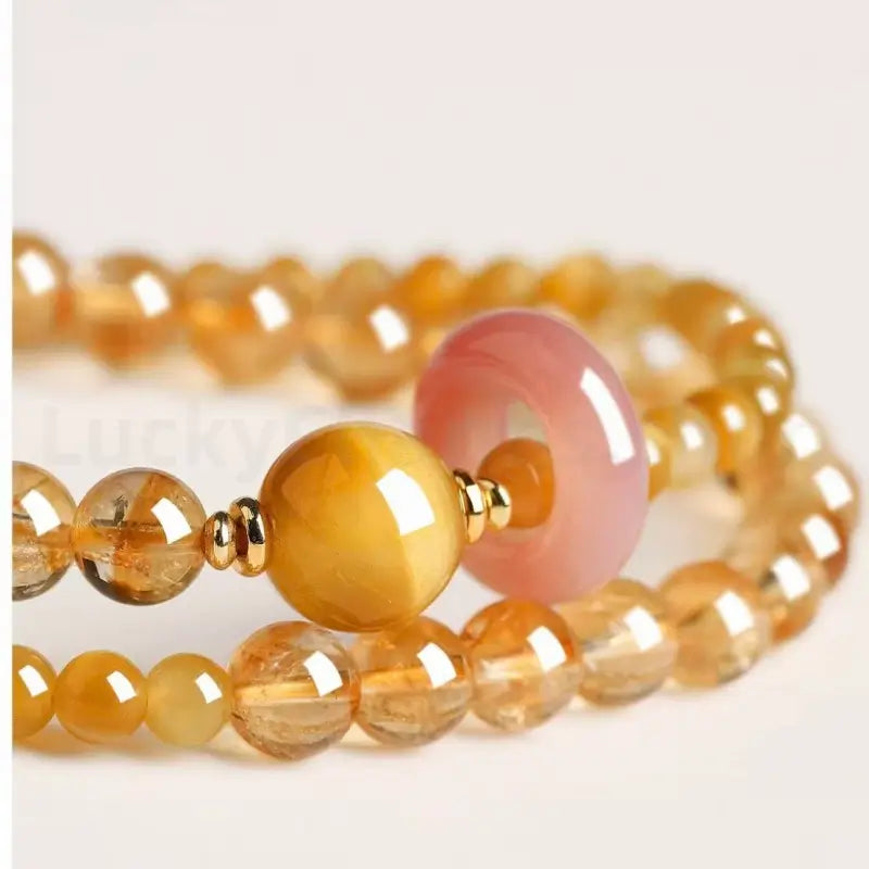 Macro macro detail of a glossy yellow chalcedony main bead and a pink quartz donut charm with gold spacer beads