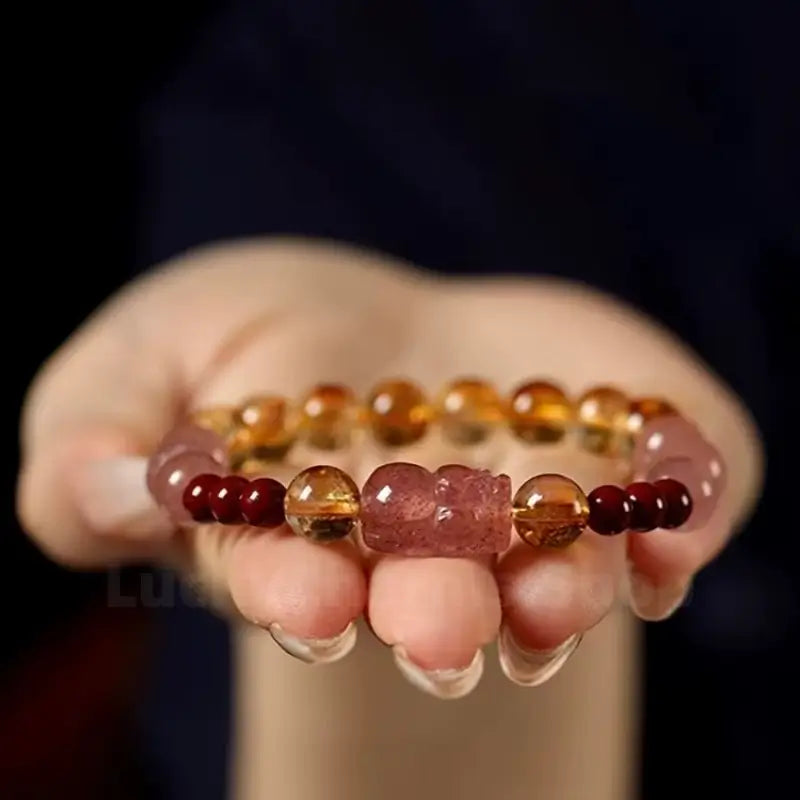 An 8mm single-strand yellow citrine gemstone bracelet featuring a pink strawberry quartz PiXiu charm held on hands