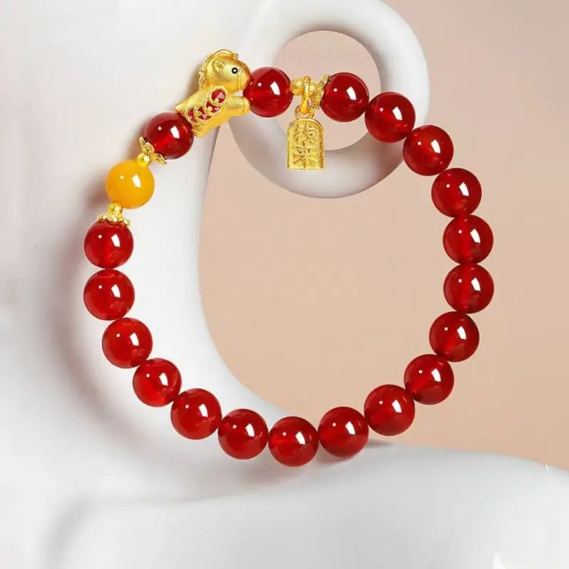 Red agate bead lucky bracelet displayed on a white stand with a gold horse charm, amber bead, and wealth tag.