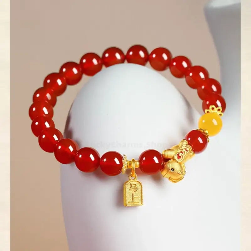 Side view of a polished red agate beaded bracelet adorned with a gold-plated horse charm and yellow bead accent.