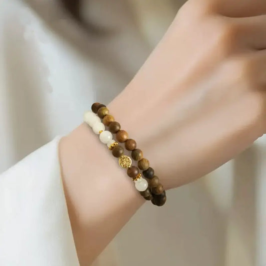 Detailed view of a beaded wealth attraction bracelet featuring glossy green sandalwood, genuine white jade beads, and an intricate golden money tree coin charm on the wrist.