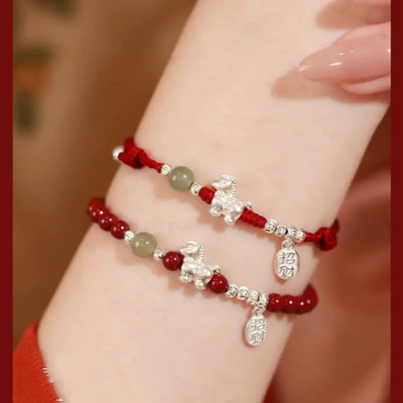 Close-up of 999 silver Horse charm red string bracelet set with natural cinnabar and jade beads on wrist.