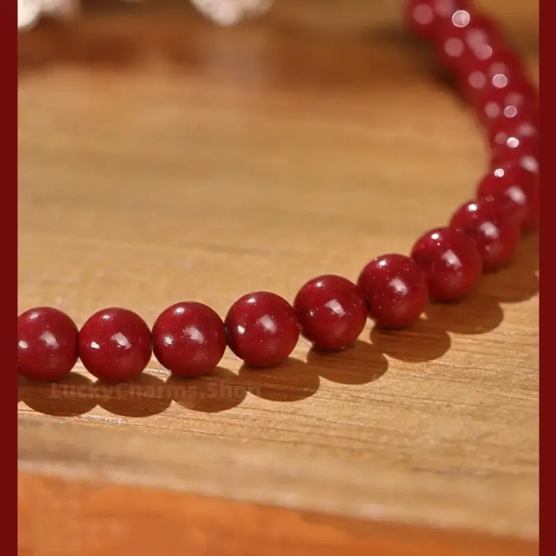 Close-up texture view of glossy natural red cinnabar gemstone beads strand resting on a smooth wooden surface.