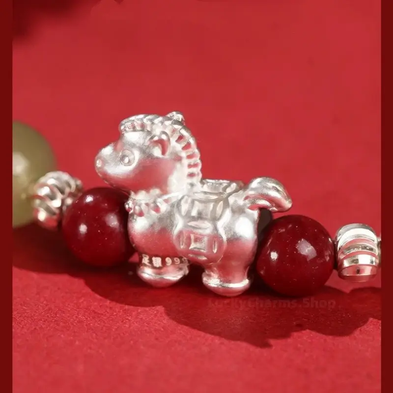 Detailed macro shot of 999 fine silver Chinese Zodiac Horse charm with coin pattern on red cinnabar bead bracelet.