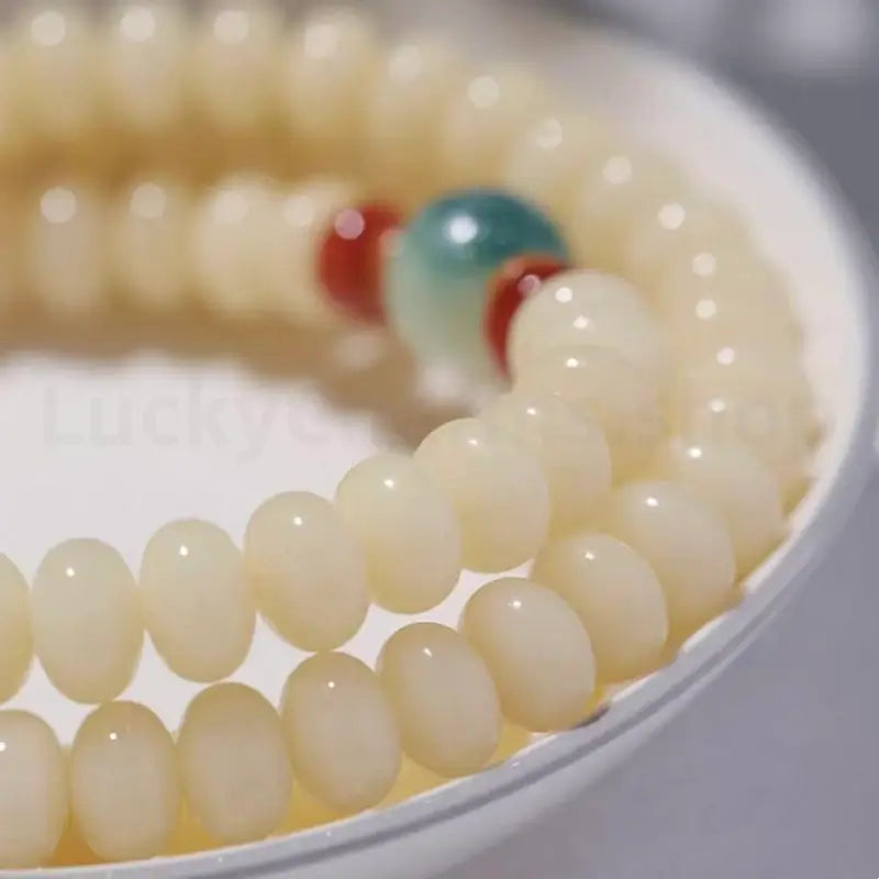 Macro shot of 6x9mm smooth white jade bodhi seed beads coiled in a white ceramic bowl, showcasing an oily jade-like luster.