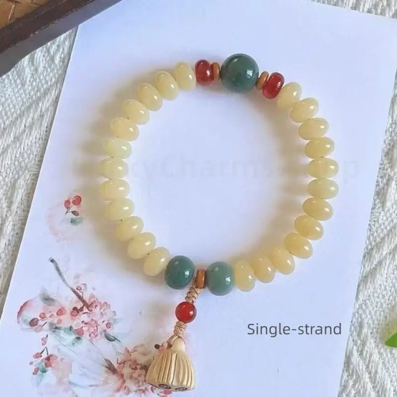 A single-strand white jade bodhi bead bracelet with a wooden lotus seedpod charm, displayed on a card with Chinese ink art.