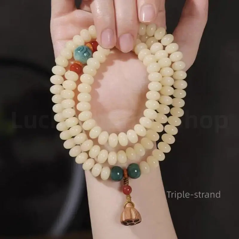 A woman holding a triple-strand white jade bodhi bead prayer bracelet in her hand, displaying how it wraps around the wrist.