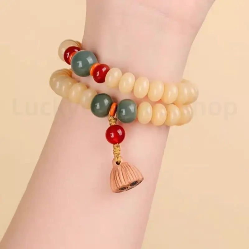 Wrist close-up of a woman wearing a double-wrap white jade bodhi seed bracelet with a wooden lotus seedpod amulet for mindfulness.
