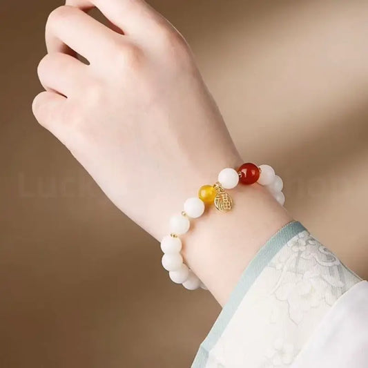 Side view of a woman wearing the white jade bodhi bead bracelet with a red carnelian charm, paired with a traditional embroidered hanfu sleeve.