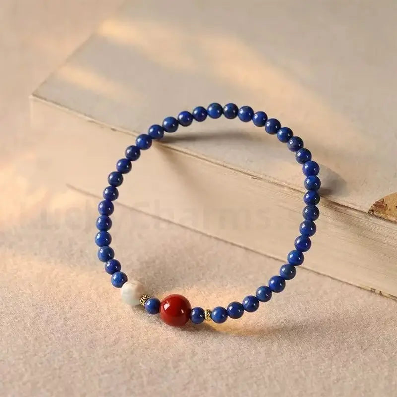 A minimalist single-strand bracelet made of 4mm blue lapis lazuli beads, featuring a prominent 8mm red cinnabar fortune bead and a pale jade accent.