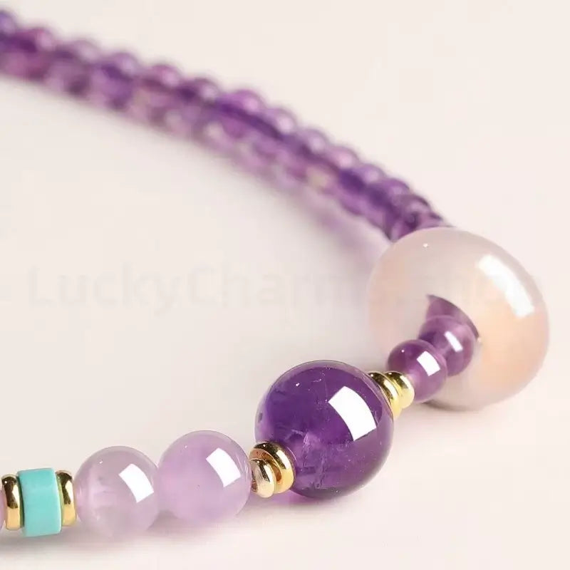Close-up detail of a natural purple amethyst bracelet showing a glossy crystal bead, gold spacers, and a turquoise accent bead