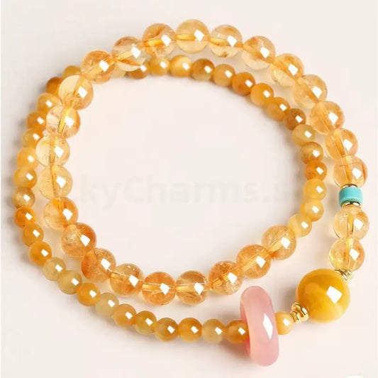 Top-down view of a multi-layer gold citrine crystal beaded wealth bracelet featuring a smooth pink chalcedony charm