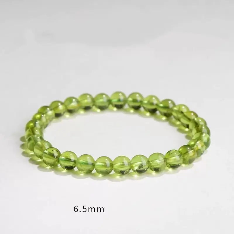 A 6.5mm natural olive green peridot beaded bracelet laid flat, labeled with "6.5mm" text to highlight the standard bead size.