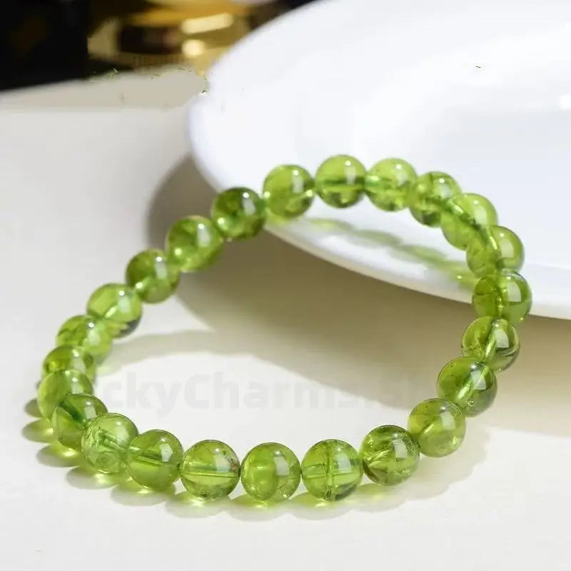 A single-strand natural peridot beaded bracelet featuring 6.5mm round crystal beads, resting elegantly in front of a white ceramic plate.