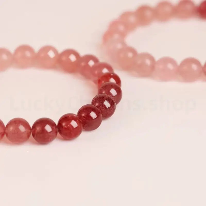 Two single-strand gradient strawberry quartz bracelets placed together, focusing on the beautiful contrast between the dark red and pale pink beads.