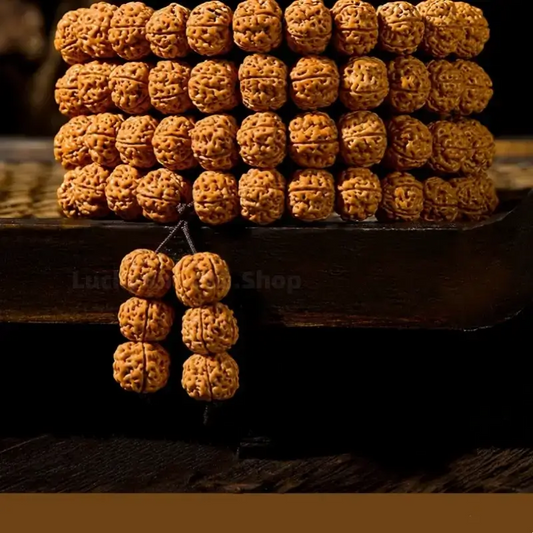 Polished 108 Rudraksha Bodhi seed mala beads neatly stacked on a vintage dark wooden tray, showcasing a smooth texture and rich golden-brown color.