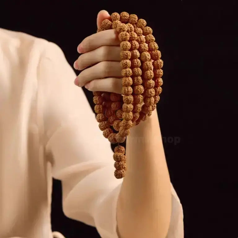 Hand holding a multi-layer Nepalese Rudraksha 108 bead prayer mala bracelet against a black background.