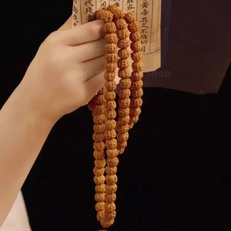 Person holding a long natural Nepalese Rudraksha 108 bead prayer necklace next to ancient scroll.