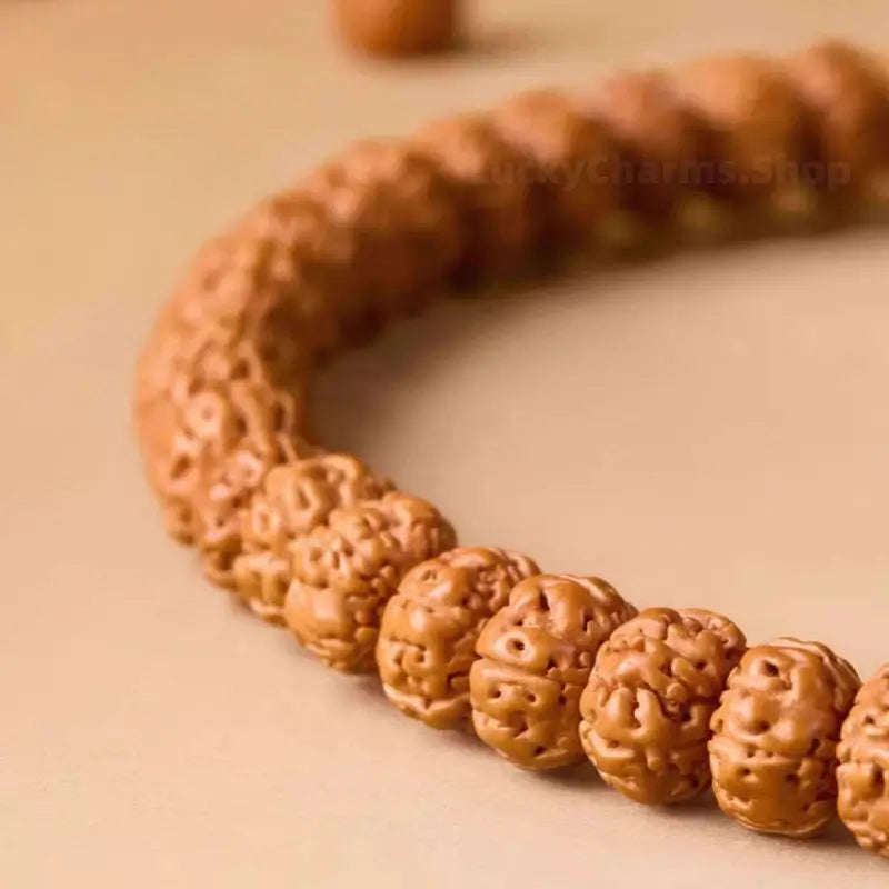 Detailed macro view of natural textured Indonesian Rudraksha mala beads strung on a beige surface.