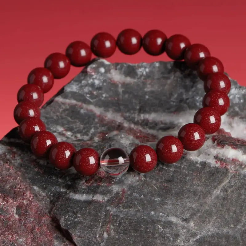 Natural cinnabar Five Elements bracelet with a clear white crystal accent bead resting on a stone surface.
