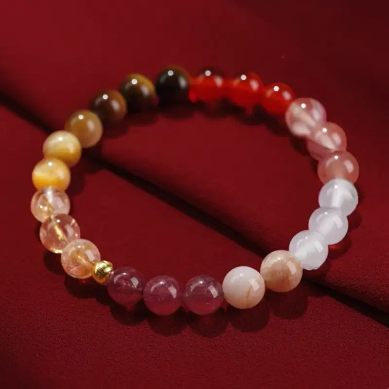 Close-up of natural multi-gemstone Five Elements balance bracelet resting on red fabric.