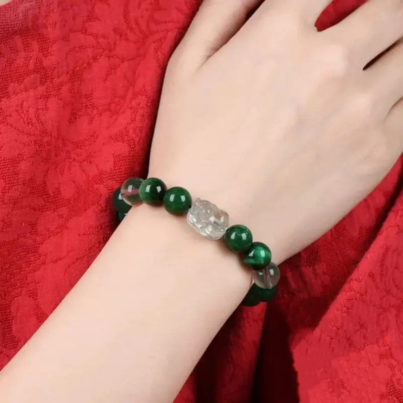 Green phantom quartz and malachite Wood element Pixiu bracelet worn on a woman's wrist over red fabric.