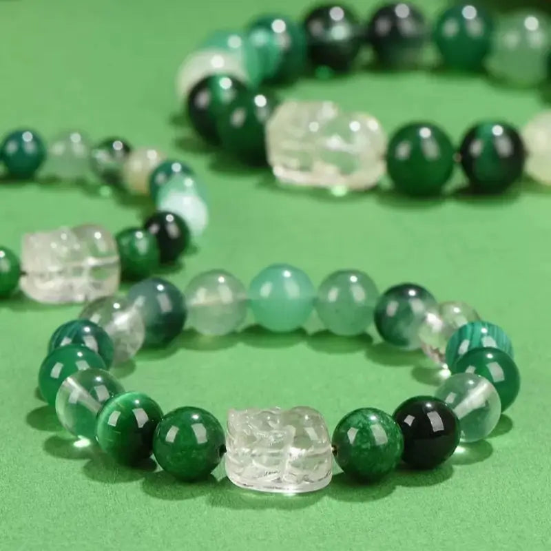 Wood element green crystal Pixiu balance energy bracelets lying on a smooth green surface.