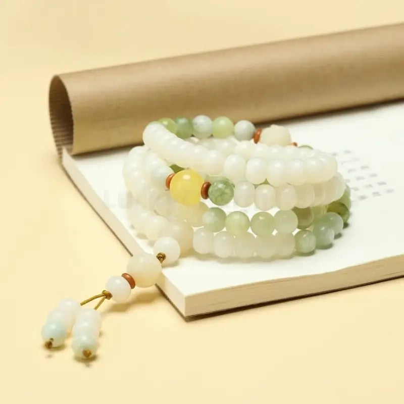 Stacked white jade Bodhi seed bracelet featuring green jadeite spacers resting on a notepad.