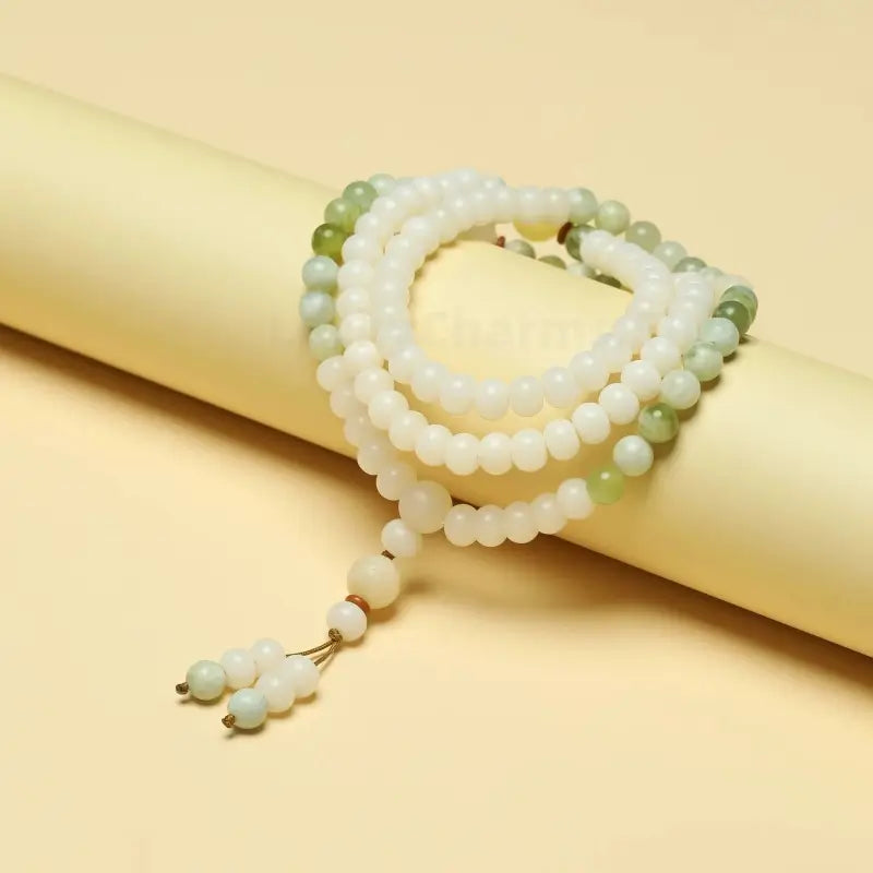 Multi-layer white Bodhi seed mala bracelet wrapped around a beige paper roll.