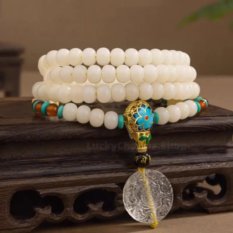 Side view of coiled white Bodhi seed prayer beads featuring cloisonné lotus accent and round crystal pendant.