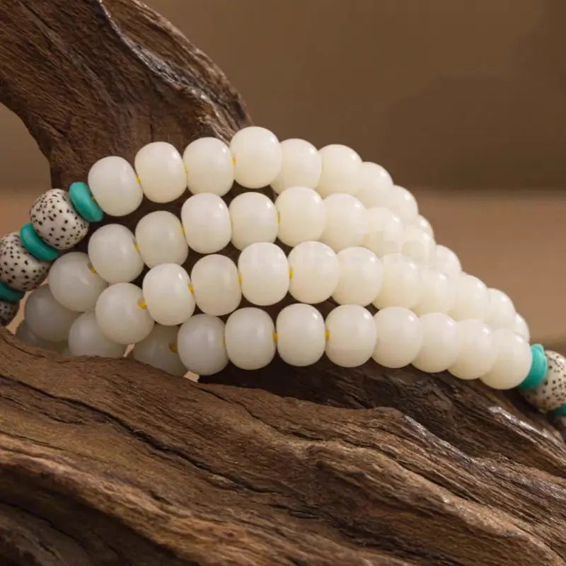 Close-up of smooth white Bodhi beads and spotted star moon Bodhi seed spacers coiled over natural driftwood.