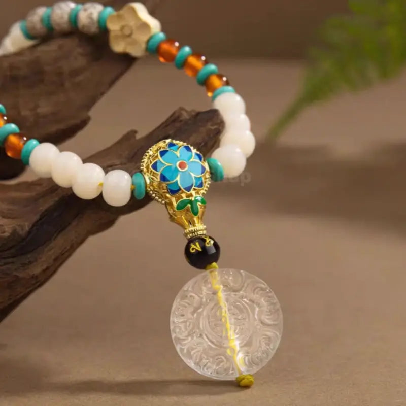 Detailed shot of blue enamel guru bead, turquoise accents, and carved white crystal amulet on a wooden branch.