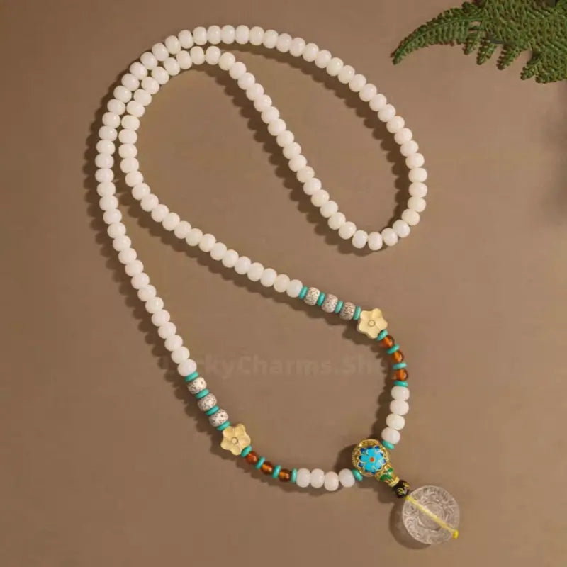 Full view of 108 white Bodhi seed mala necklace laid out flat with flower spacers and clear crystal pendant.