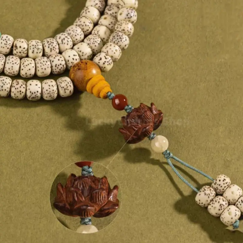 Close-up of intricate carved sandalwood lotus charm and yellow gourd bead on Bodhi seed mala.