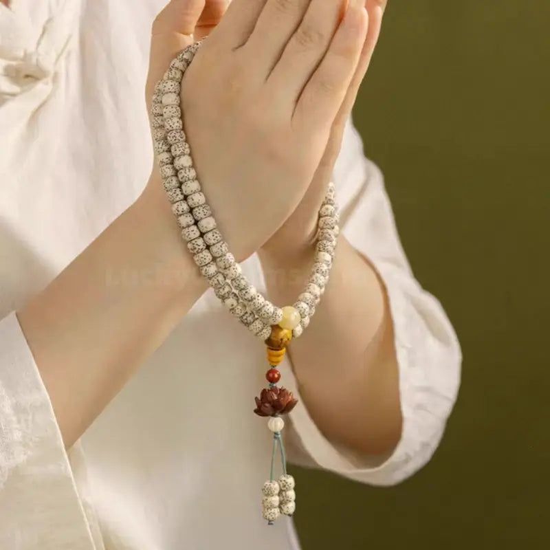 Person holding star moon Bodhi seed prayer beads with sandalwood lotus pendant in praying hands.