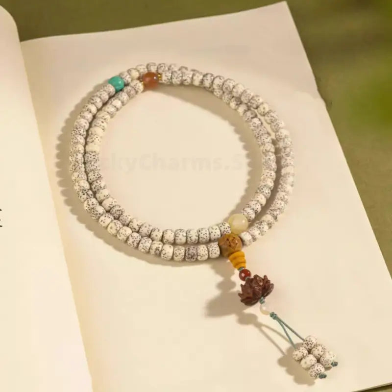 Coiled star moon Bodhi seed mala bracelet with sandalwood lotus pendant resting on an open book.