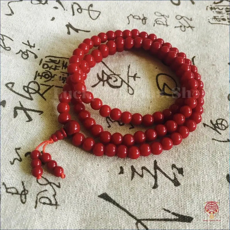 Coiled red prayer beads mala strand with tassel on traditional calligraphy fabric.