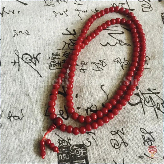 Top view of a red six-conduit wood mala prayer necklace for meditation and chanting on traditional fabric.