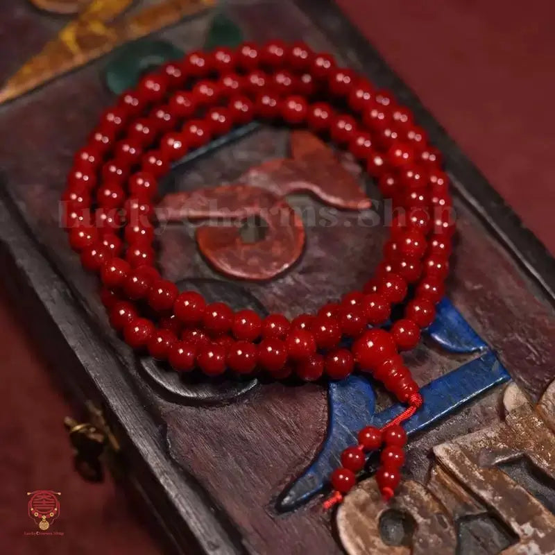 Deep red mala prayer beads coiled on a carved Tibetan wooden prayer box.