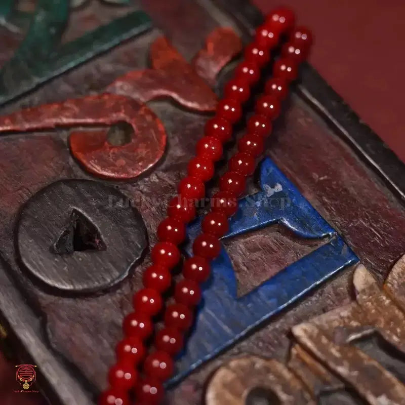Close-up of glossy red prayer beads resting on vintage carved wooden box with characters.