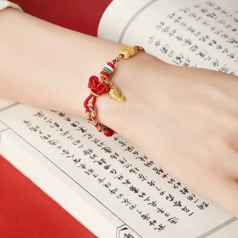 Multicolored woven koi fish charm bracelet resting on a hand over a traditional calligraphy book.
