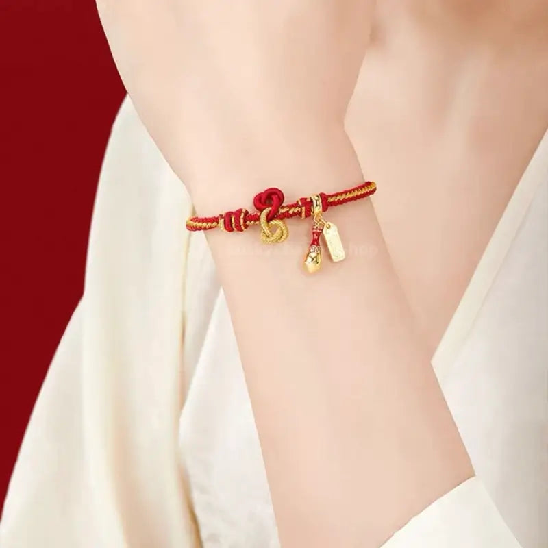 Woman wearing red and gold hand-woven lucky bracelet with calligraphy brush charm on wrist.