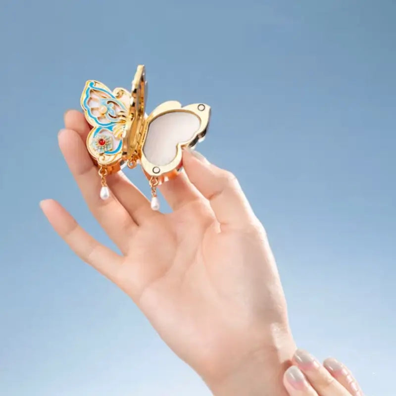 Hand holding opened gold butterfly solid perfume compact showing fragrance balm inside.