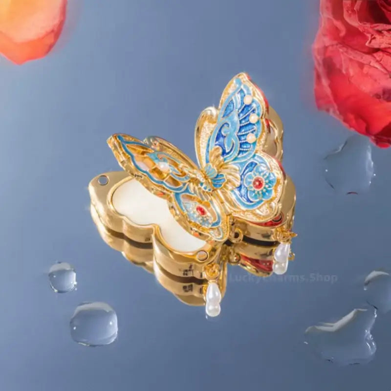 Opened gold and blue enamel butterfly solid perfume compact reflected on mirrored surface.