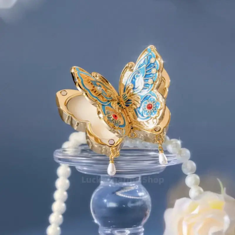 Butterfly solid perfume compact with pearl dangles on glass stand with pearl necklace.