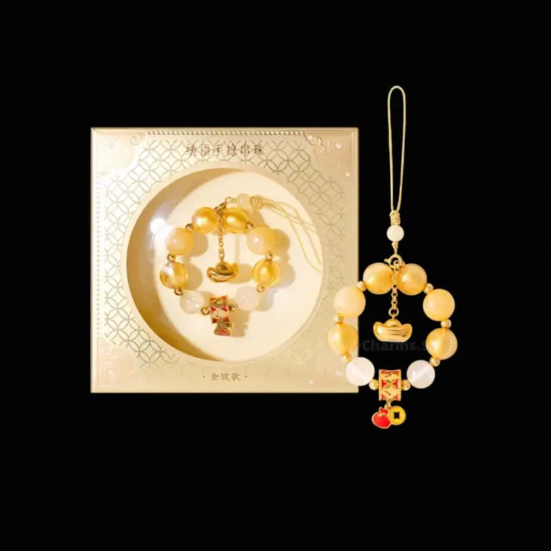 Palace Museum yellow citrine beaded phone charm next to its gold decorative gift box.