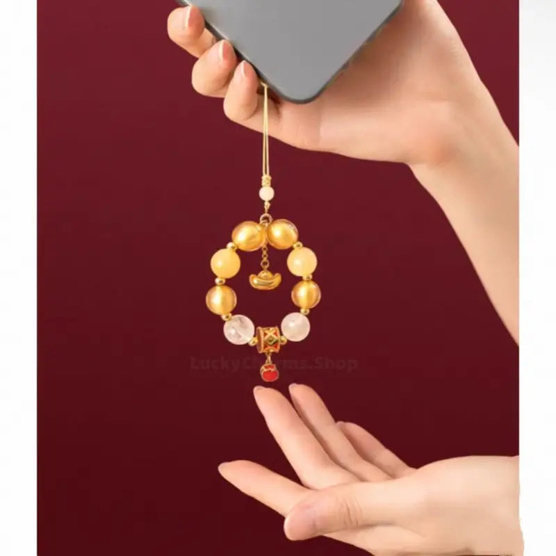 Hand holding yellow agate beaded phone strap attached to a phone with gold ingot pendant.